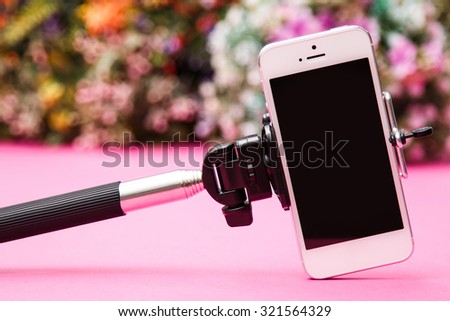 Smart phone and selfie stick on background with flowers
