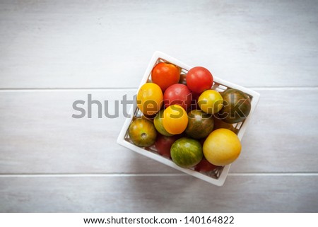 Green, red and yellow Heirloom tomatoes in a white container on a white good background with a light vignette
