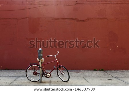 Red biked locked to a parking meter in front of a red painted wall