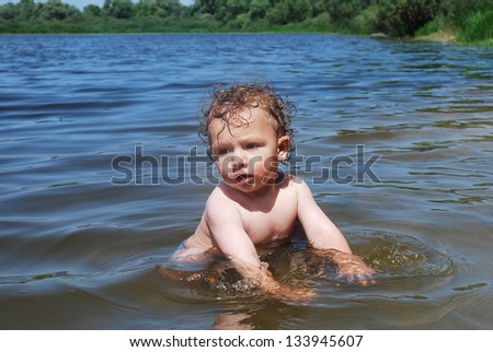 In the summer, a little curly-haired boy swimming in the river.