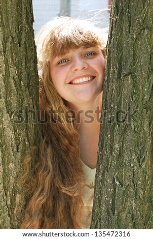 In the summer, a beautiful girl with long curly hair peeking from behind a tree