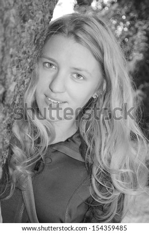In the summer, the girl looks out from behind a tree. Black-and-white photography.