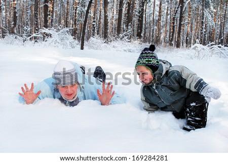Winter mother with her son indulge lie on the snow in the woods, a bright sunny day
