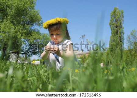 Little girls sitting in a field in spring wreath of dandelions.