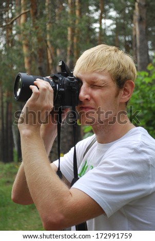 Paparazzi. Unshaven man with a camera in the summer forest.