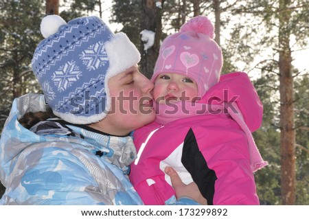 Mom kissing baby daughter in a snowy pine forest.