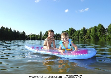 In summer, the river indulge boy and a girl, they float on an inflatable mattress.