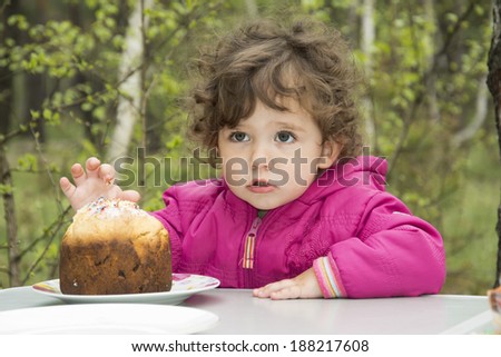 Little curly girl on picnic in the woods trying cupcake.