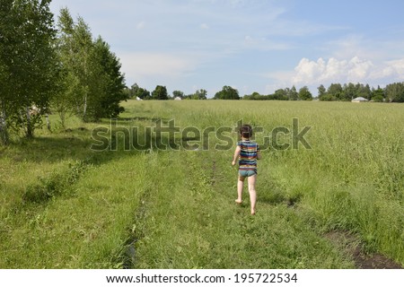 Rural barefoot boy running down the road in a field near birches.