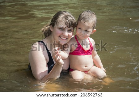 Summer smiling mother with little funny daughter swimming in the river.