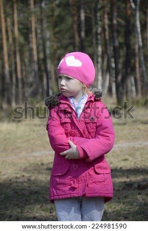 Little angry upset girl in a pink jacket stands alone in the spring forest.