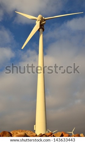 Perspective from below of towering wind turbine  on blue sky and clouds