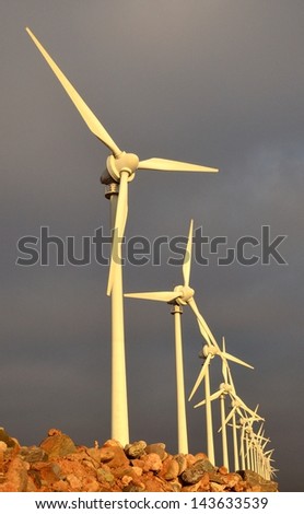 Vertical image with perspective from below of modern wind turbines in perfect alignment on gray clouds background