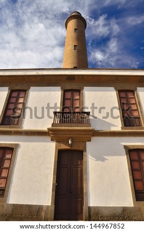 Perspective view from below of the main entrance of lighthouse building with wood  windows, stone structure and front door in woodwork, clouds and blue sky, Maspalomas, Gran canaria