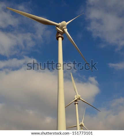Towering modern generators of electric energy in aeolian park with its vanes to the wind, on blue sky and clouds