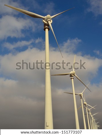 Perspective image of towering wind generators on blue sky and clouds