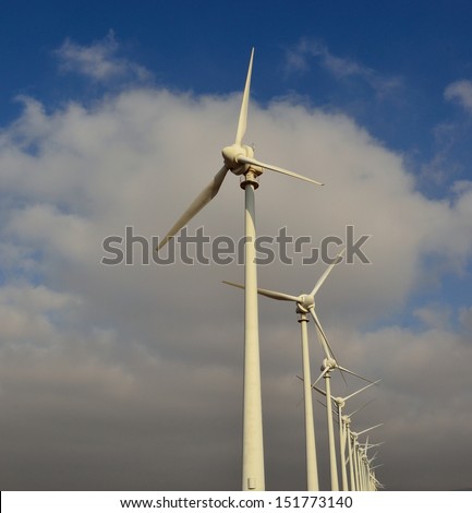 Modern wind turbines in aeolian park for industrial production of electric energy, on blue sky and clouds background