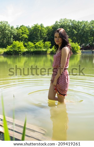 Brunette stands knee-deep in water in the middle of the lake. Girl enjoying the cool water on a hot summer day. Girl, lake, cool, sun - concept holiday. The idea of ??an article on summer vacation.