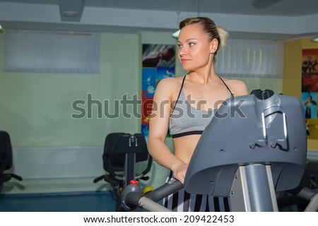 The beautiful blonde in the gym. The coach stands on the treadmill. Girl shows exercise. Treadmill, fitness, running, healthy living, trainnings - The concept of health. Article about the sport.
