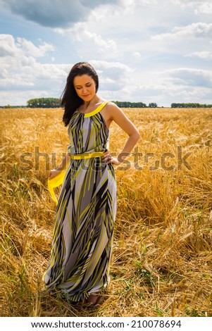 Young brunette woman in a dark dress. A girl stands in the middle of a wheat field on a sunny day. Field, wheat, beauty, nature, relaxation - The concept of country vacation. Article about vacation.