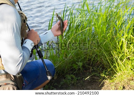 Fisherman in professional gear on the river bank. Fisherman catching fish and holds it in his hand. Pike, fish, fishing, nature, fishing rod - the concept of leisure. Article about fishing.