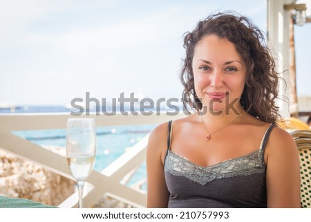 Beautiful curly brunette in cafe. Girl in a cafe on the beach enjoying life. Beauty, happy, sea. The concept of sea side holiday. Article about sea vacatiion