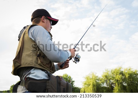 Fisherman on the river bank. Man fisherman catches a fish. Fisherman in his hand holding spinning. Fishing, spinning reel, fish, Breg rivers. - The concept of a rural getaway. Article about fishing.