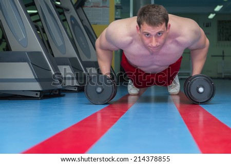 Man at the gym. Man makes exercises. Sport, power, dumbbells, tension, exercise - the concept of a healthy lifestyle. Article about fitness and sports.