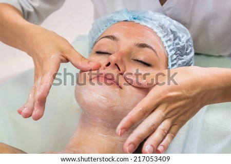 Hands of therapist apply cream to face of woman. Concept of care and youth.Girl with a beautician at spa salon.Cosmetology, facial, beauty. Article about cosmetology.