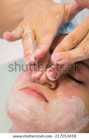 Hands of therapist apply cream to face of woman. Concept of care and youth.Girl with a beautician at spa salon.Cosmetology, facial, beauty. Article about cosmetology.