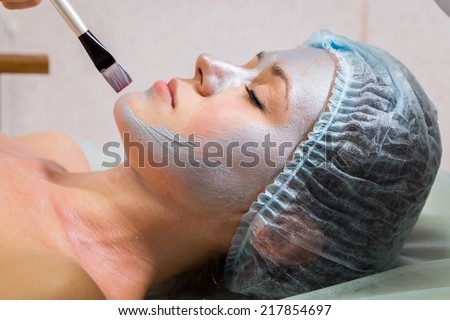 Spa therapy for young woman receiving facial mask at beauty salon - indoors.Beautiful woman with facial mask at beauty salon.Woman with clay facial mask in beauty spa