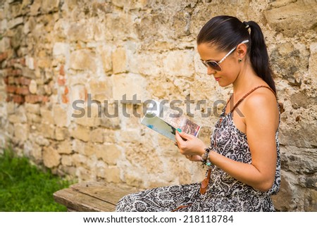 Female holding a map outdoors.The girl in the ancient city. Brunette sitting on a background of an old brick wall and looking at the map. Travel, an ancient city, historical sites - Travel Concept.