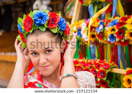 Young, beautiful Ukrainian girl in a wreath of flowers. Portrait of a beautiful girl in the fresh air. Girl stands near shops with souvenirs