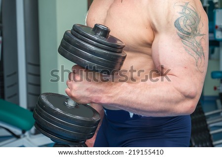 Athletic man doing exercise with dumbbells n the gym. Man makes exercises. Sport, power, dumbbells, tension, exercise - the concept of a healthy lifestyle. Article about fitness and sports.