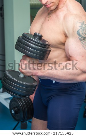 Athletic man doing exercise with dumbbells n the gym. Man makes exercises. Sport, power, dumbbells, tension, exercise - the concept of a healthy lifestyle. Article about fitness and sports.