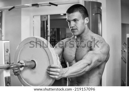 Male athlete in the gym. Athlete athletic clothes heavy shell on the barbell. Sport, power, dumbbells, tension, exercise - the concept of a healthy lifestyle. Article about fitness and sports.