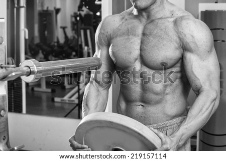 Male athlete in the gym. Athlete athletic clothes heavy shell on the barbell. Sport, power, dumbbells, tension, exercise - the concept of a healthy lifestyle. Article about fitness and sports.