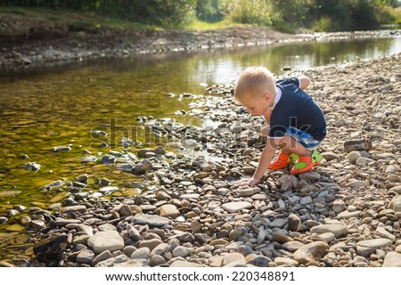Cute three year old boy throwing stones to the water outdoor on a summer day.Little boy on the river.Kids Games, river, childhood, pebbles, carefree, fun - the concept of children to play outdoors.
