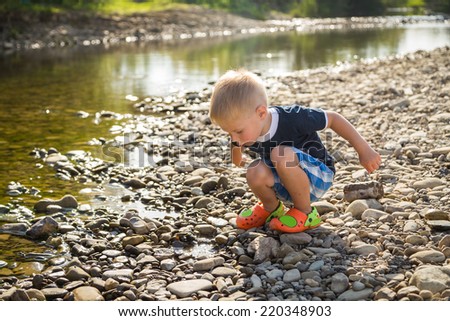 Cute three year old boy throwing stones to the water outdoor on a summer day.Little  on the river bank.Kids Games, river, childhood, pebbles, carefree, fun - the concept of children to play outdoors.