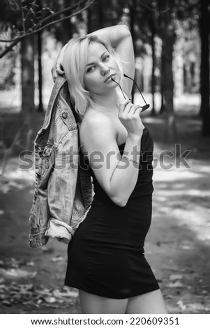 Blonde with sun glasses in the woods.Blonde in the forest.Young attractive woman in a romantic autumn scenery. Blonde woman posing in forest.Girl with jacket in hand and trees on background.