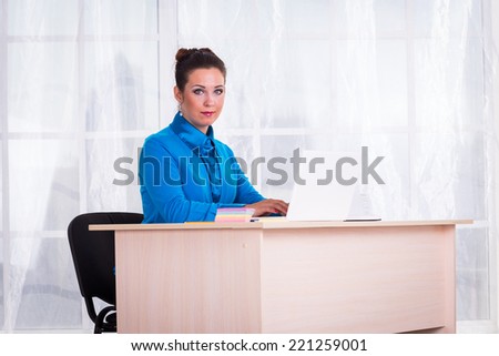Business woman working in the office at the table.young business woman reading sitting at the desk on office background.Portrait of businesswoman with laptop writes on a document at her office