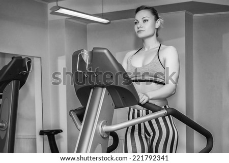 The beautiful blonde on a treadmill. Black and white photography.Cute young woman exercising on a treadmill at a gym.Attractive young fitness model runs on a treadmill,is engaged in fitness sport club