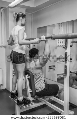 Gym man exercising with his personal trainer.Man with his personal fitness trainer in the gym exercising with athletic Rod.Sport, power,dumbbells tension,exercise - the concept of a healthy lifestyle.
