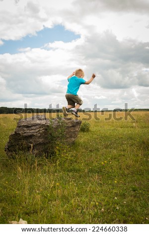 Kid playing outdoors. Boy jumping from stone. Kid hangs in the air jumping from stone. overcoming fears.Childhood, games, prigat, fresh air, carelessness - the concept of childhood.