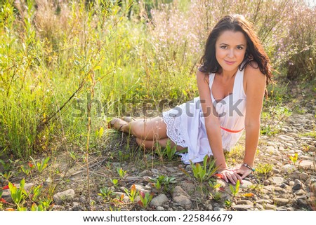Young brunette woman in a white dress. A girl stands in the middle of pink flowers field on a sunny day. Field, flowers beauty, nature,  - The concept of country vacation. Article about vacation.