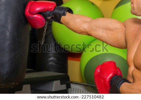 Muscular man in the gym. The man in red boxing gloves, hit a punching bag, exercise. Boxing, workout, muscle, strength, power - the concept of strength training and boxing