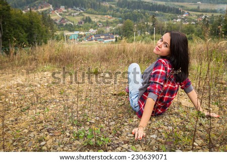 Brunette girl in casual clothes on nature. The girl has a rest on a hillside, she sits and stares dreamily into the distance. Hiking, mountain, leisure, nature - the concept of mountain travel.