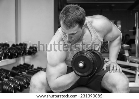Handsome muscular man working out with dumbbells in gym.Sport, power, dumbbells, tension, exercise - the concept of a healthy lifestyle. Article about fitness and sports.