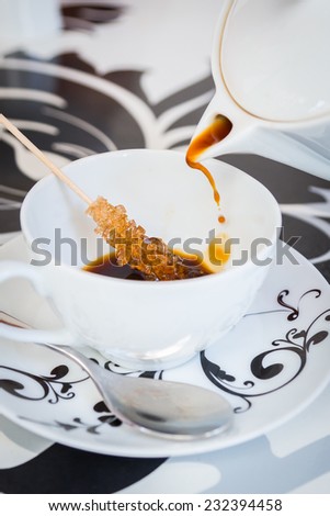 Coffee from a beautiful black and white teapot, pour into a cup on the table designer. Stick with sugar remain in the cup. Coffee, tea, mug, pour, caffe - the concept of catering.