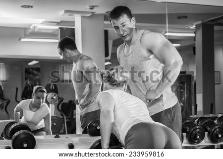 Man and woman trained in the gym. Trainer demonstrates exercises, girl. Loving couple in the gym. Family fitness, exercise, coaching - team work in the gym.